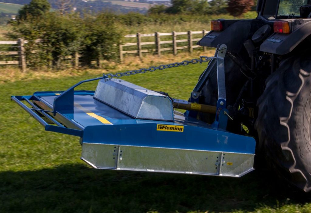 A blue tractor with a 9 FT HEAVY DUTY IN LINE FLEMING TOPPER on a green field was seen.